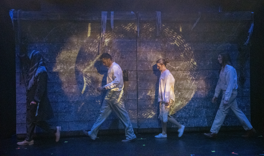Theatre production with three men on stage walking to left